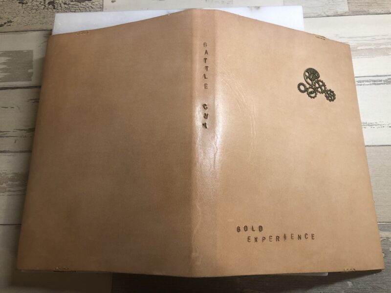ベージュ色のヌメ革で出来たブックカバーの背表紙に「BATTLE CRY」と刻印されている３